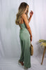 Blonde girl models crossback cami jumpsuit in color sage for Scarlette The Label, an online fashion boutique for women. Paired with a large straw bag and nude heels. 
