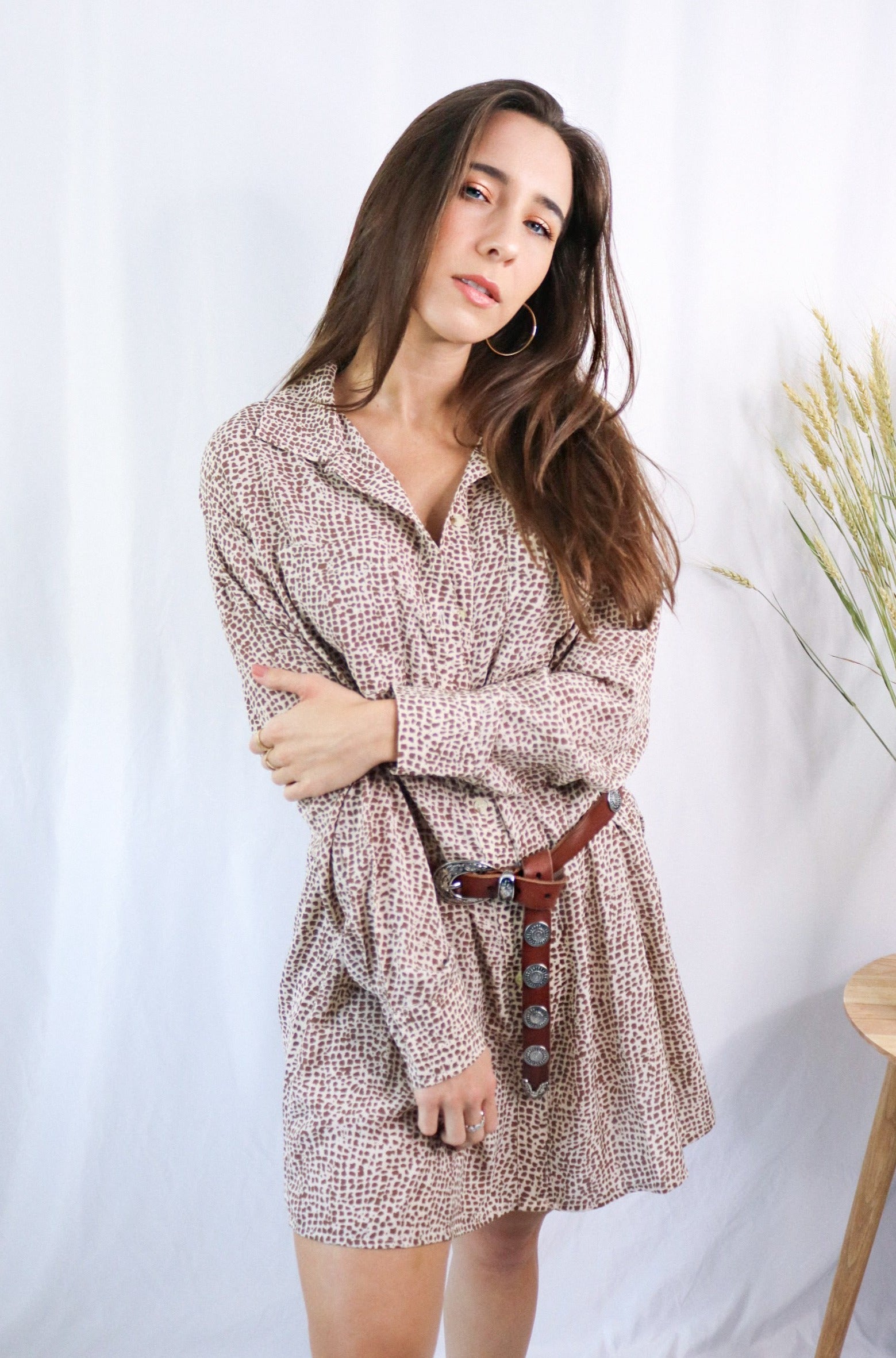 Brunette girl models a collared T-Shirt Dress in Animal Print (cheetah / leopard print). The t-shirt dress is collared, brown, and mid-length. It is a long sleeve t-shirt dress with a loose and comfortable fit and paired with a brown belt.