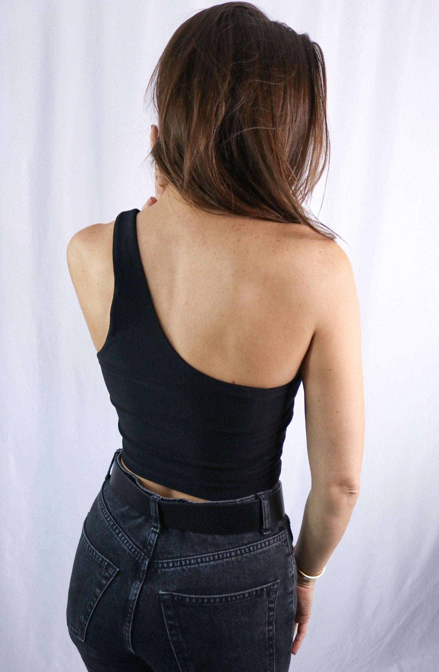 Brunette girl models a black one shoulder crop top for Scarlette The Label, an online fashion boutique for women. The black one shoulder crop top is double lined. Paired with dark denim jeans.