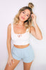 Blonde girl models the Namaste Home Loungewear Collection set for Scarlette The Label, an online fashion boutique for women. The set includes a soft white crop top and baby blue loungewear shorts. Sold separately.