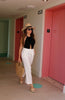 Black halter keyhole openback bodysuit from Scarlette The Label, an online fashion boutique for women. Paired with white pants, a large straw handbag and a wide brimmed hat.