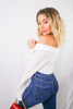 Load image into Gallery viewer, Blonde girl models an off the shoulder long sleeve button down shirt in white for Scarlette The Label, an online fashion boutique for women. The white button down shirt is tied as a crop top. Paired with dark denim jeans and a red and gold clutch. 