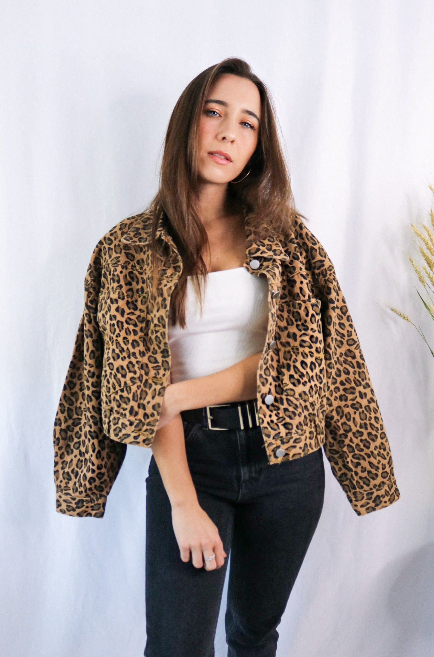 Brunette girl models a buttoned leopard jacket for Scarlette The Label, an online fashion boutique for women. Paired with white ribbed spaghetti strap tank top in white and dark denim jeans.