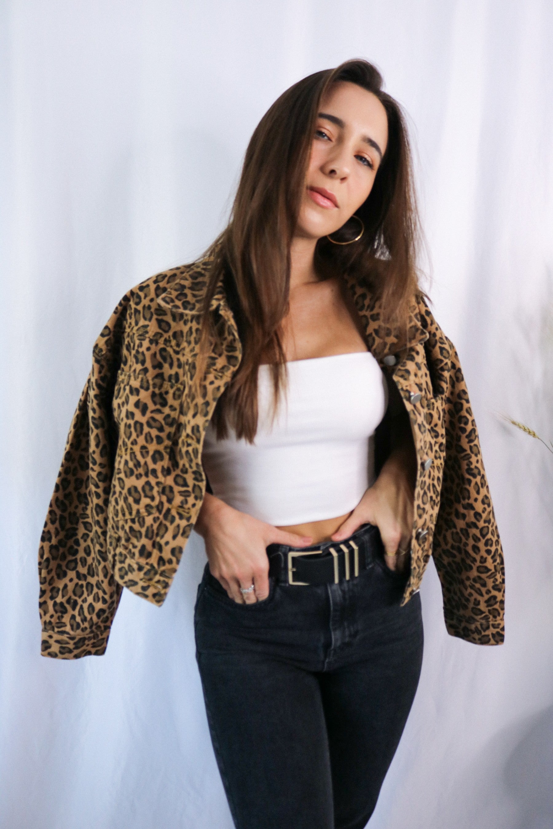 Brunette girl models a buttoned leopard jacket for Scarlette The Label, an online fashion boutique for women. Paired with white ribbed spaghetti strap tank top in white and dark denim jeans.