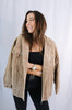 Brunette girl models buttoned corduroy jacket in the color tan for Scarlette The Label, an online fashion boutique for women. The corduroy jacket is an oversized street style jacket. Paired with a black crop top, dark denim jeans.