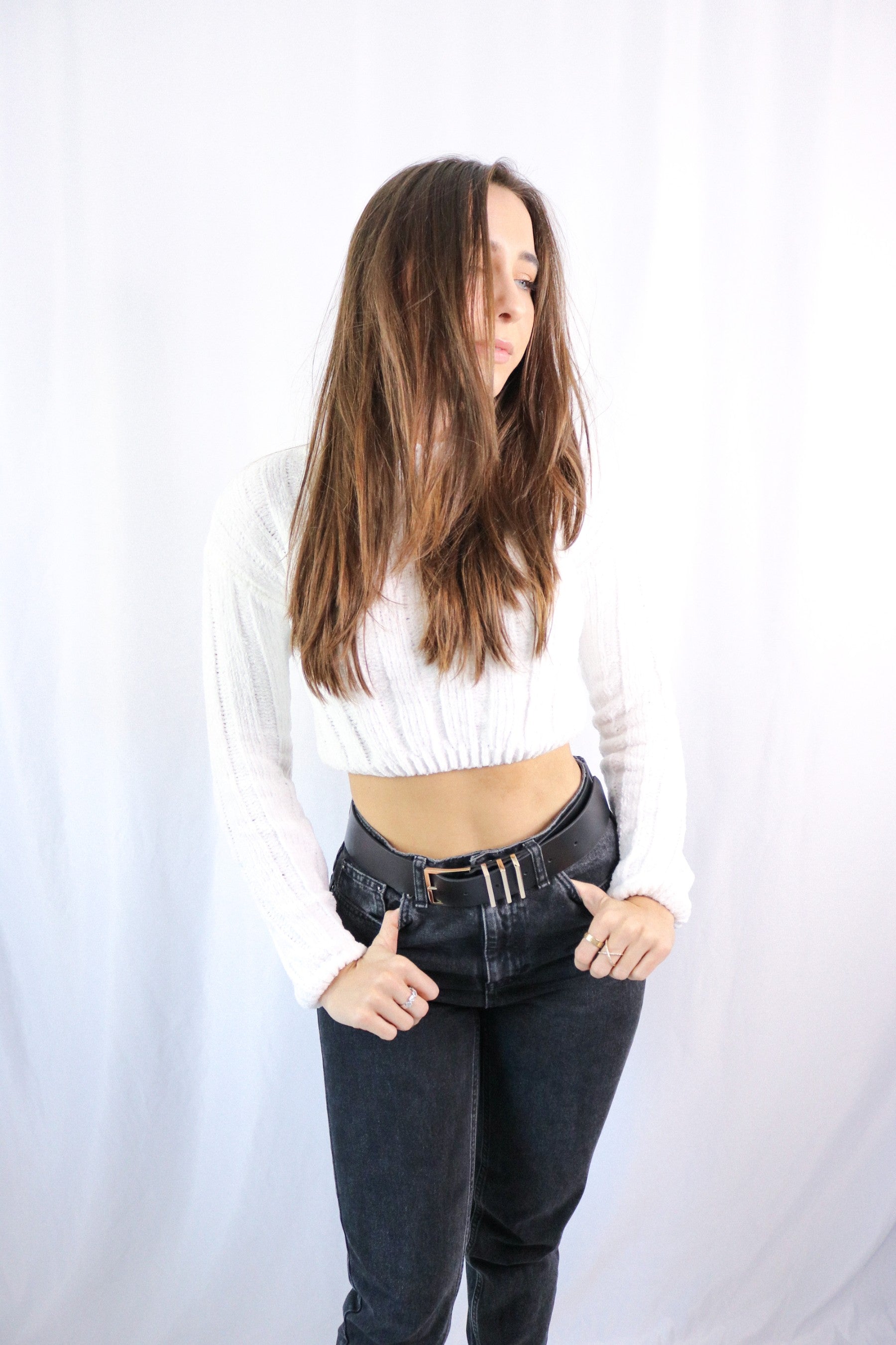 Brunette girl models ivory (white) knitted crop sweater for Scarlette The Label, an online fashion boutique for women. THe knitted crop sweater is very soft and breathable. Paired with dark denim jeans.