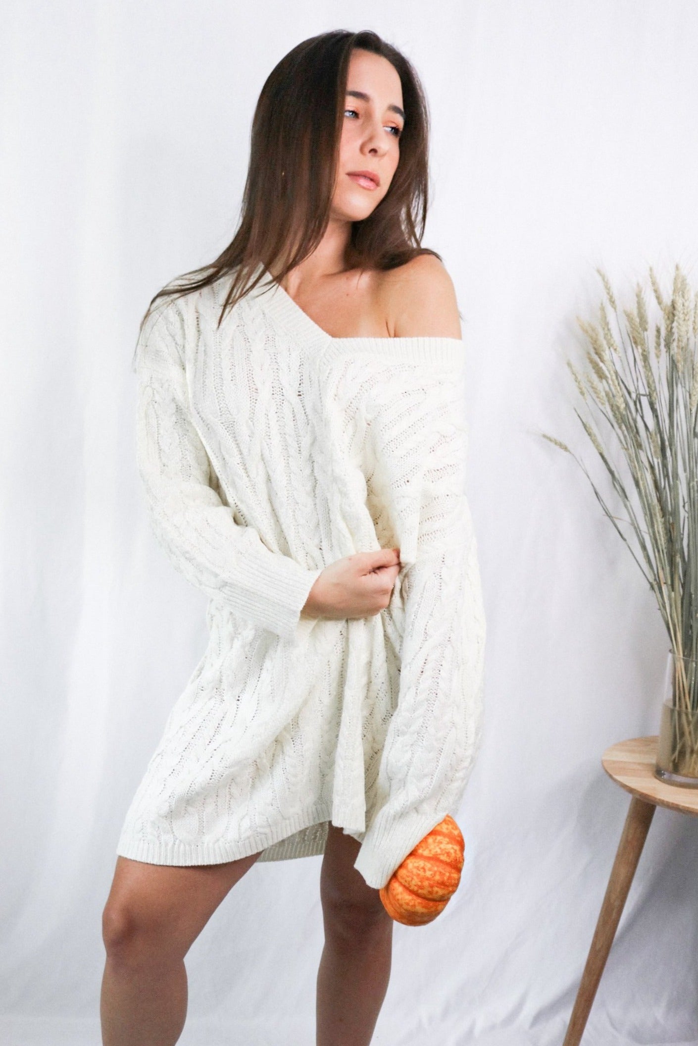 Brunette girl models a mid-length cable knit sweater dress in the color ivory for Scarlette The Label, an online fashion boutique for women. 