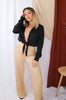 Load image into Gallery viewer, Blonde girl models long sleeve low plunge tie bodysuit in black for Scarlette The Label, an online fashion boutique for women. Paired with wide leg flare beige ivory pants.