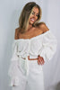 Load image into Gallery viewer, Blonde girl models an off the shoulder frilled blouse in white for Scarlette The Label, an online fashion boutique for women. Paired with white, wide-leg pants.
