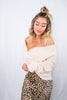 Blonde girl modeling an off the shoulder , twist front sweater in the color cream for Scarlette The Label, an online fashion boutique for women. Paired with a midi leopard maxi skirt.