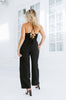 Load image into Gallery viewer, Blonde girl models black crossback jumpsuit with pockets for Scarlette The Label, an online fashion boutique for women. Paired with black heels.
