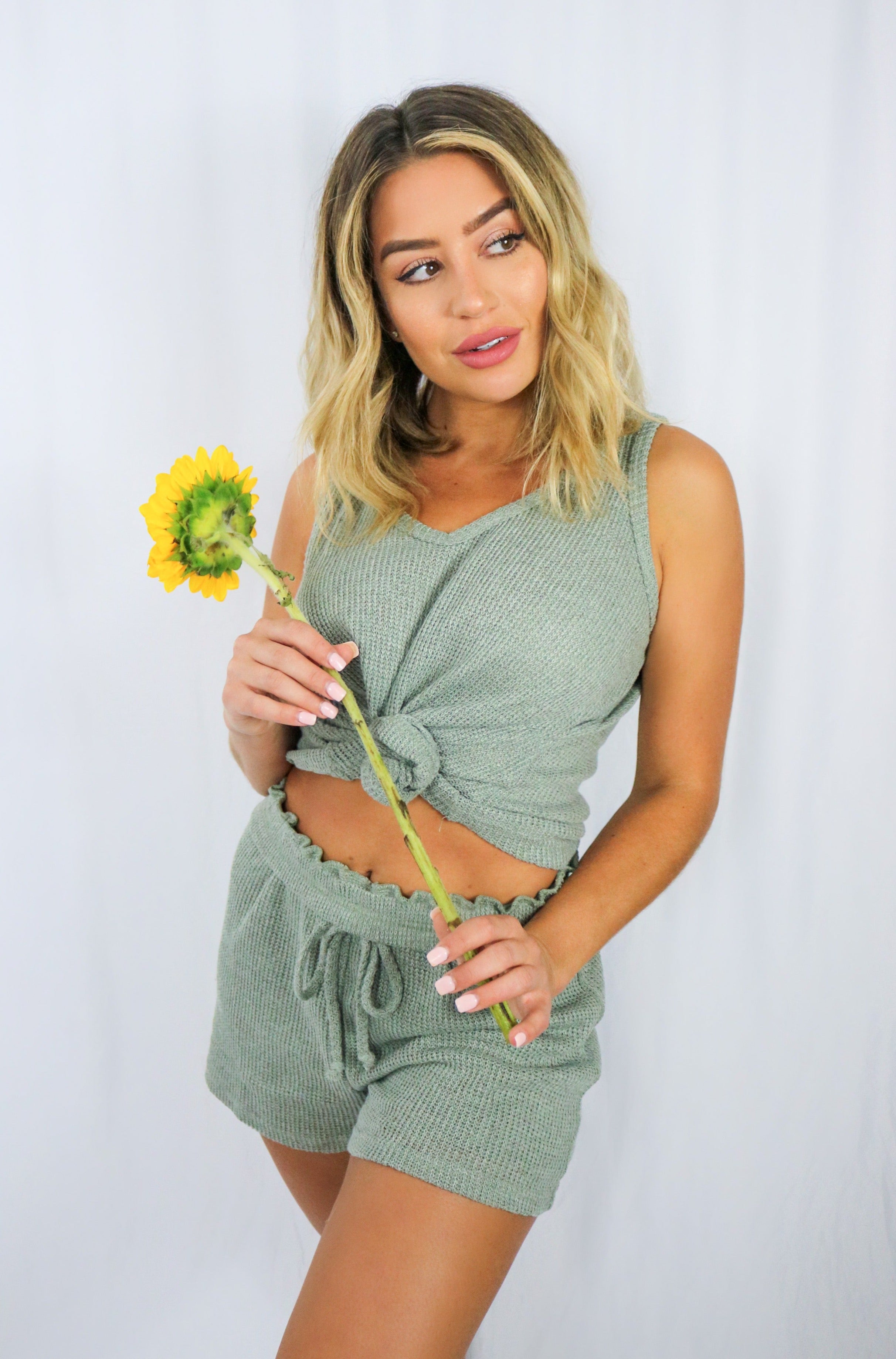Blonde girl models knitted loungewear short set in color olive for Scarlette The Label, an online fashion boutique for women. 