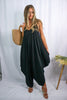 Blonde girl modeling a black boxy hi lo jumpsuit for Scarlette The Label, an online fashion boutique for women. Black jumpsuit has pockets and is lightweight and flowy. Paired with large straw bag.