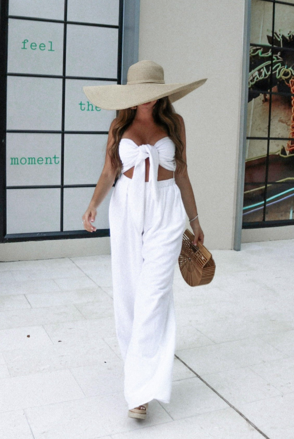 100% Cotton Linen Vacation Pant Matching Set in White with tie tube top and matching flowy wide leg pants.  Paired with wooden handbag and big floppy hat. Scarlette The Label, online fashion boutique for women. Staycation Collection SS 2021.