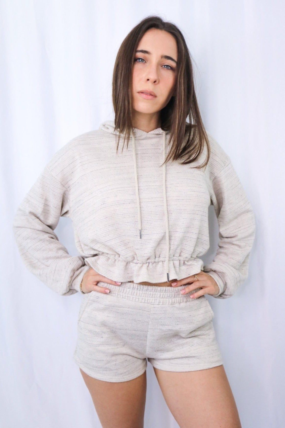 Brunette girl models a long sleeve hooded loungewear short set in color: natural for Scarlette The Label, an online fashion boutique for women.