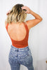 Load image into Gallery viewer, Blonde girl models a plain ponte bodysuit in the color rust for Scarlette The Label, an online fashion boutique for women. Paired with dark denim jeans and a beige wide-brimmed rancher hat.