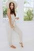 Brunette girl models beige tie jumpsuit for Scarlette The Label, an online fashion boutique for women. Paired with a beige wide-brimmed rancher hat.