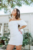 Load image into Gallery viewer, Brunette girl models white ruched mini dress with puff sleeves for Scarlette The Label, an online fashion boutique for women. White mini dress can be worn off the shoulders or regular.