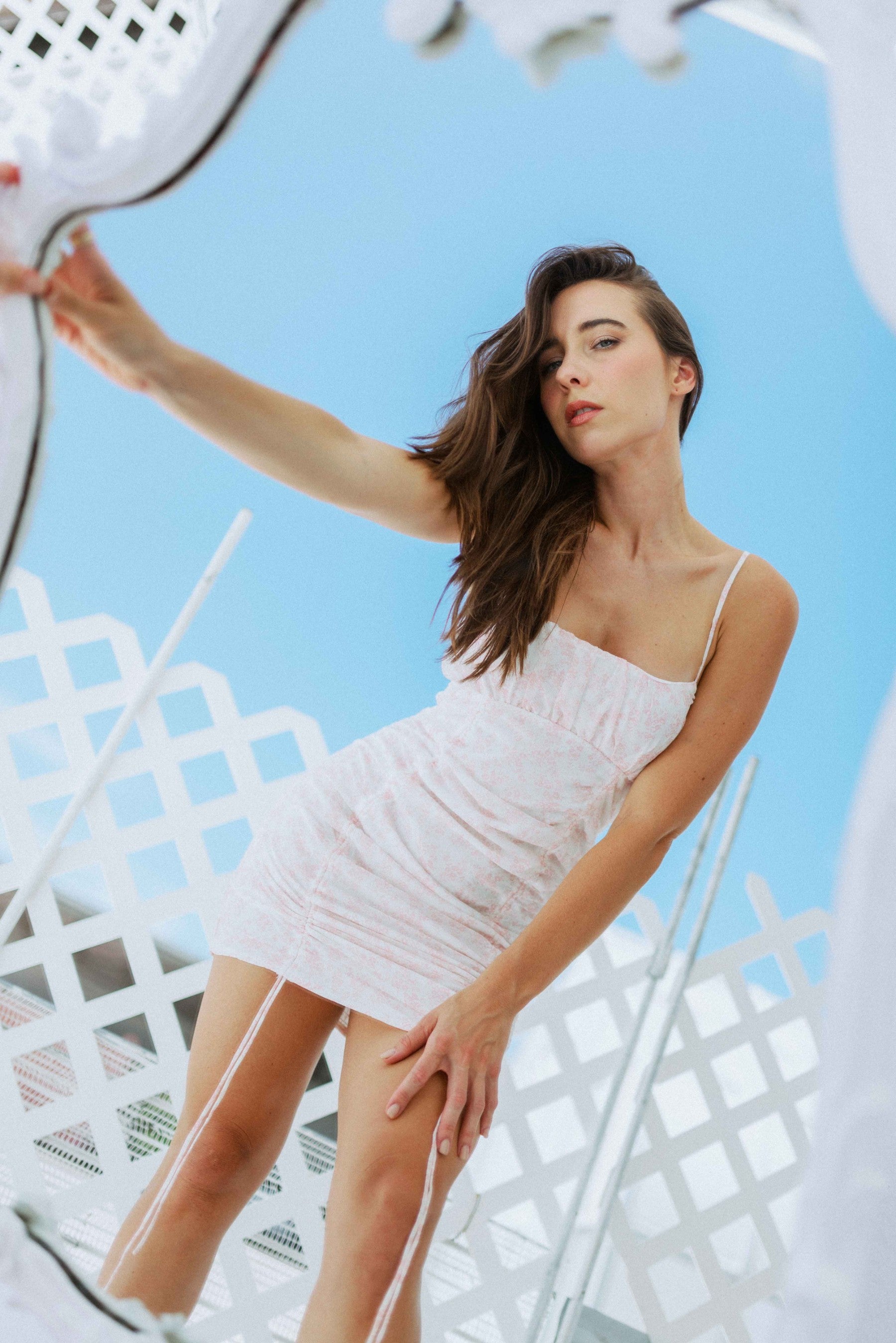 Brunette girl models a scrunched mini dress for Scarlette The Label, an online fashion boutique for women. The mini dress is a spaghetti strap mini scrunched dress in white with soft pink details.