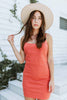 Brunette girl models a solid orange spaghetti strap mini dress for Scarlette The Label, an online fashion boutique for women. The orange mini dress is paired with a wide-brimmed rancher hat.