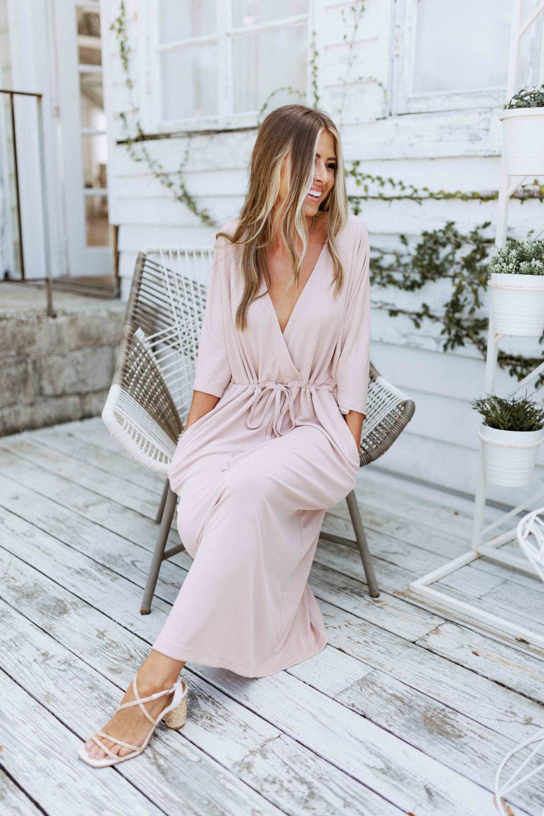 Blonde girl models a plunging neckline maxi dress in the color mauve for Scarlette The Label, an online fashion boutique for women. Plunging neckline maxi dress has adjustable waist strings.