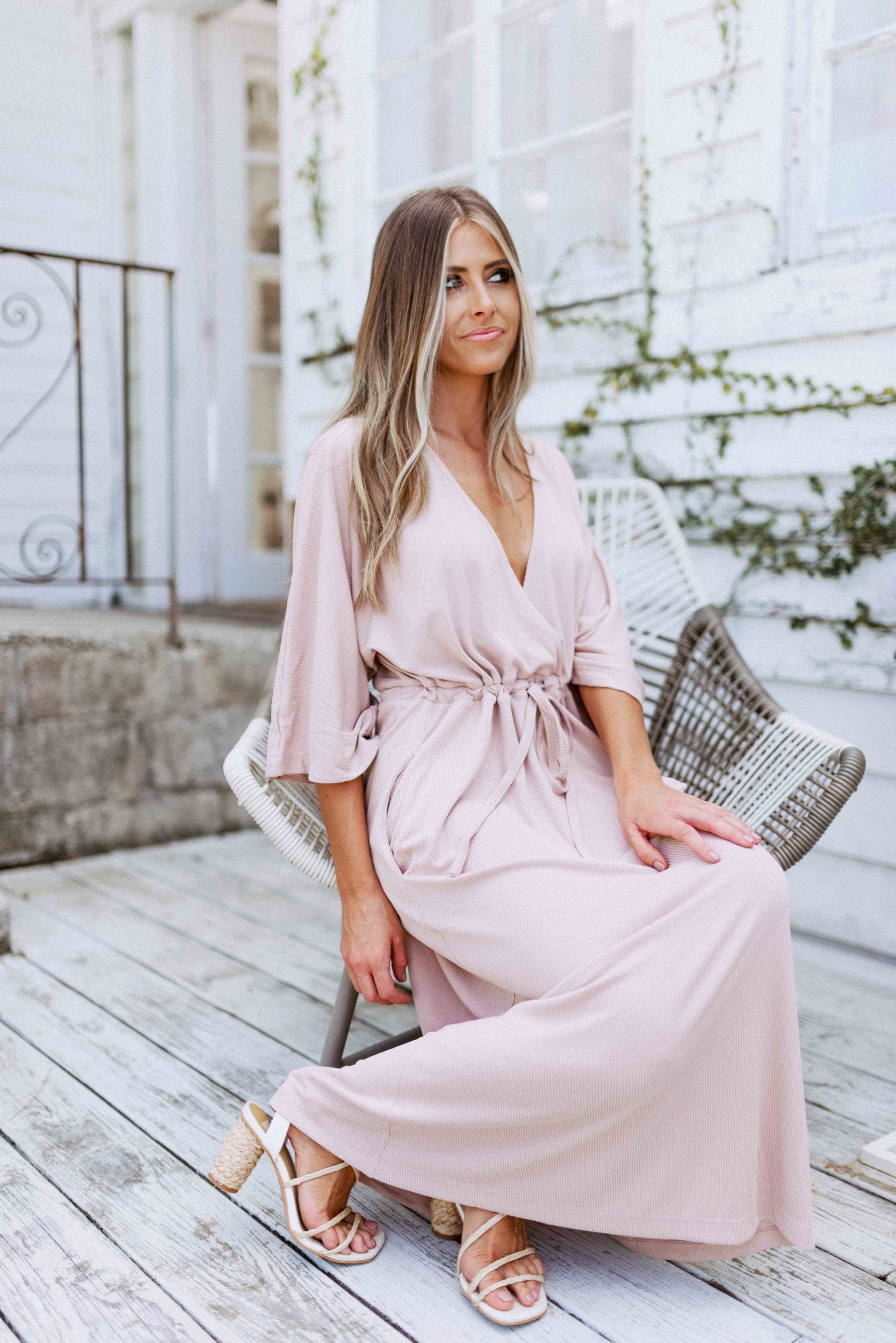 Blonde girl models a plunging neckline maxi dress in the color mauve for Scarlette The Label, an online fashion boutique for women. Plunging neckline maxi dress has adjustable waist strings.