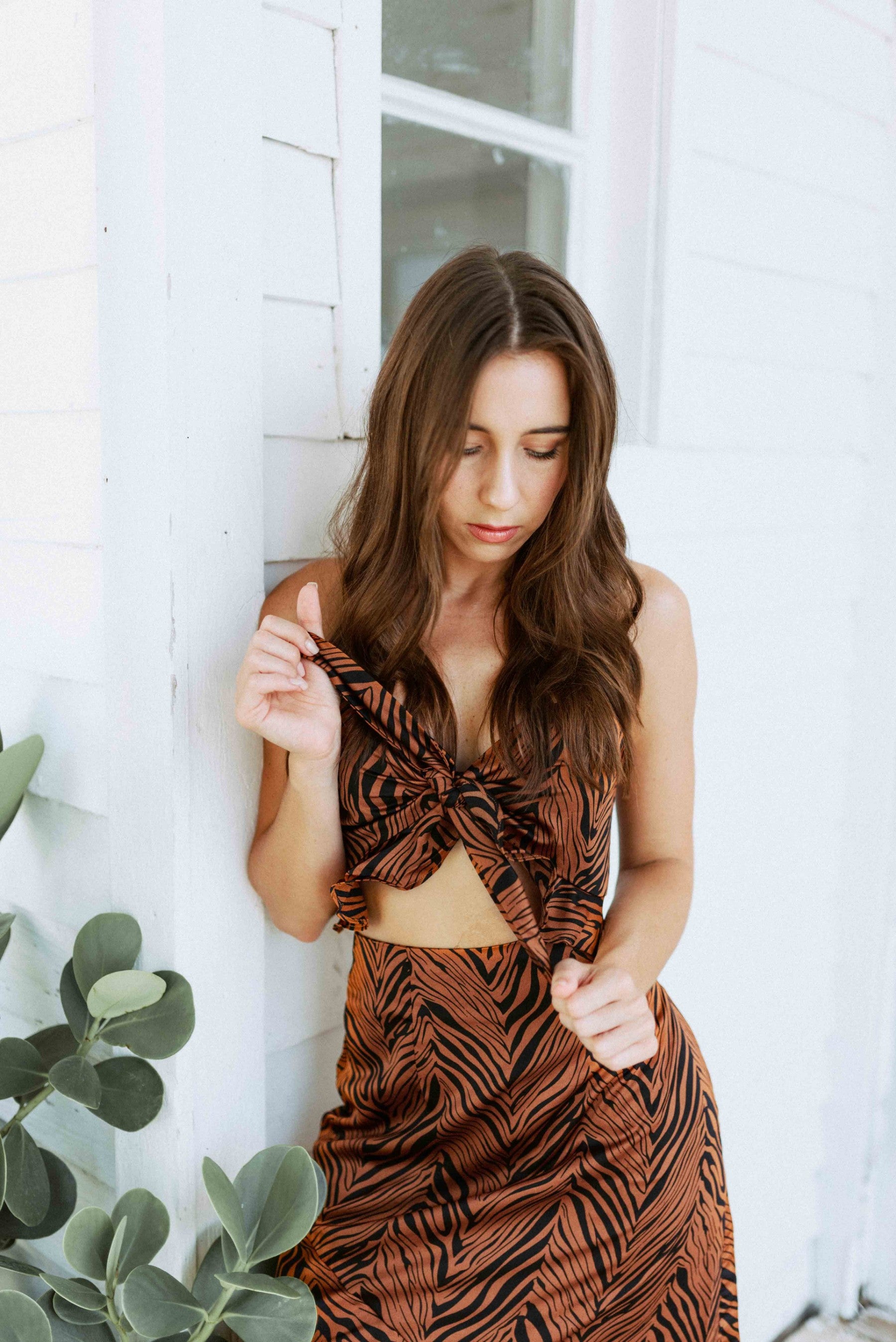 Brunette girl models an animal print maxi skirt set in brown and black. The matching maxi skirt set comes with a spaghetti strap crop top and long, flowy maxi skirt.