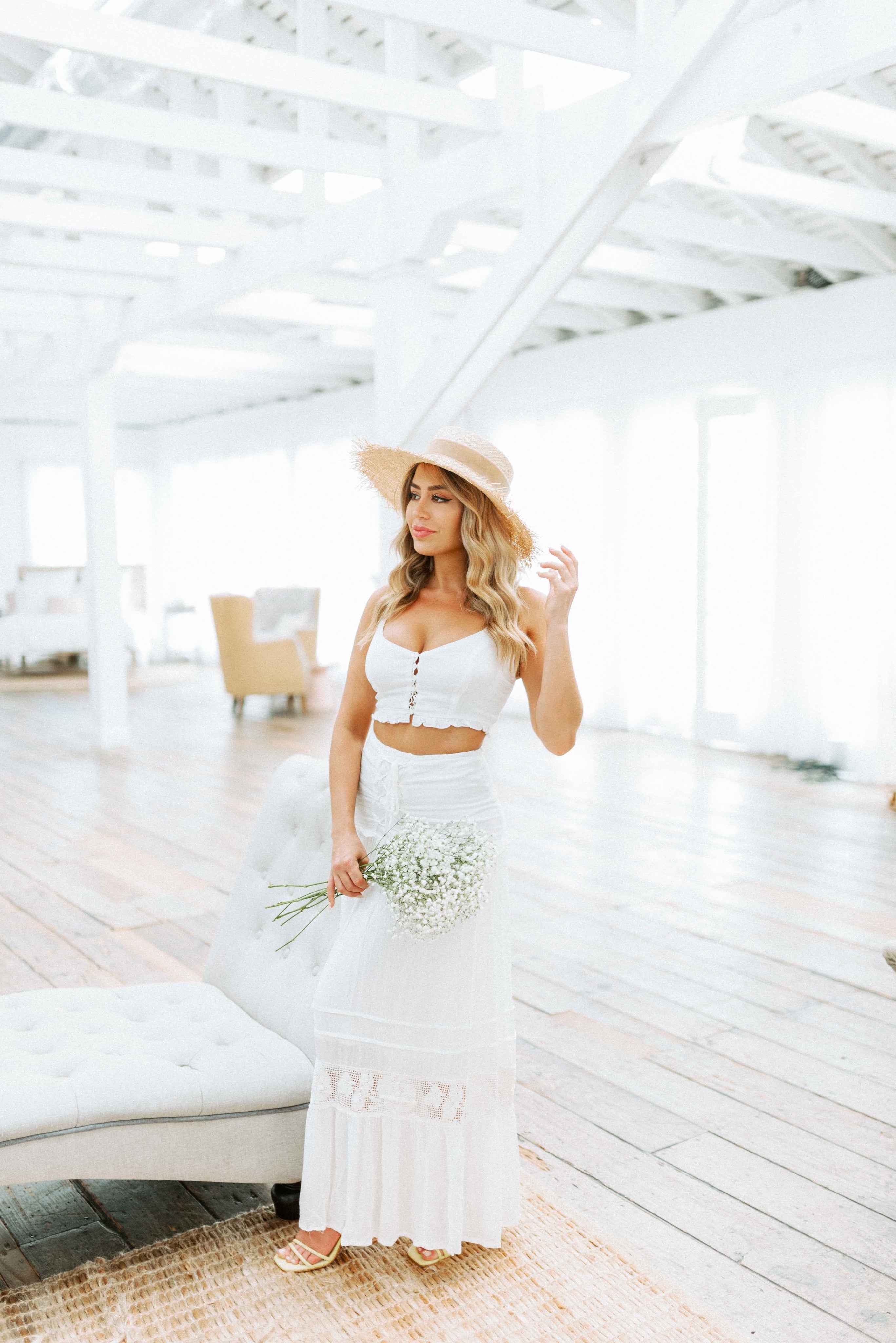 Blonde girl models white matching skirt set for Scarlette The Label, an online fashion boutique for women. The matching set includes a white frilled crop top and a white long, flowy, maxi skirt.