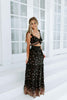 Load image into Gallery viewer, Blonde girl models black frilled maxi skirt set in black for Scarlette The Label, an online fashion boutique for women. The matching skirt set includes a black tie crop top and  black, long, flowy maxi skirt. Floral details.