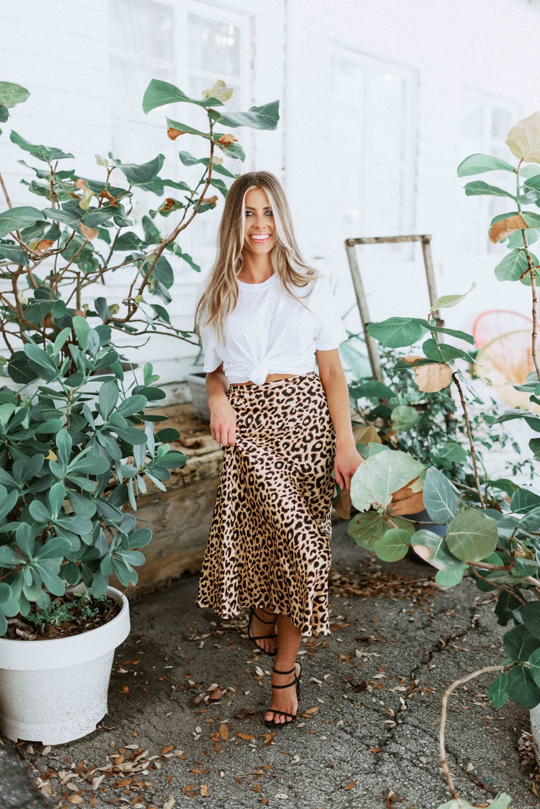 Blonde girl models midi skirt in leopard print for Scarlette The Label, an online fashion boutique for women. Midi leopard print skirt paired with a plain white tee and black heels.