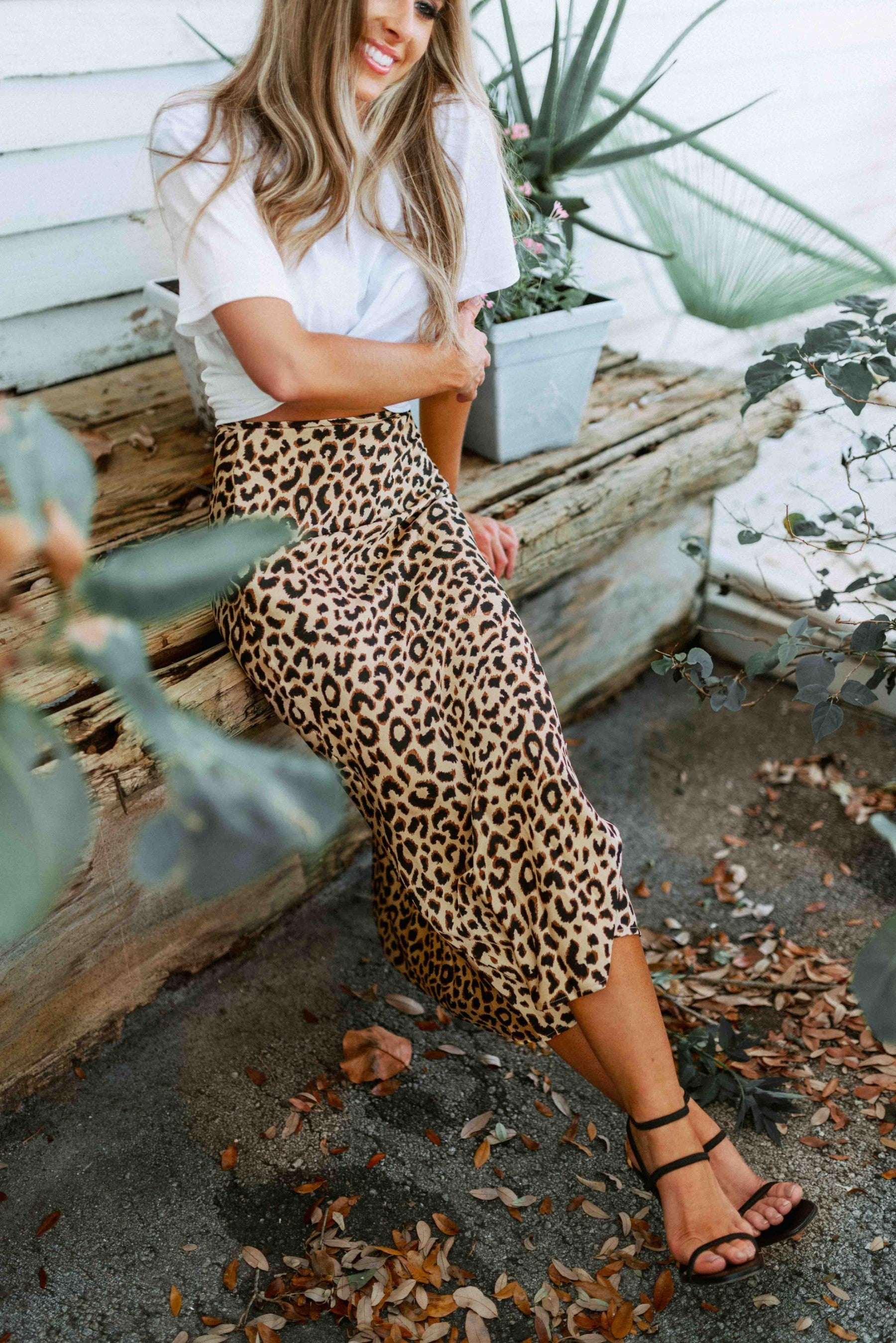 Blonde girl models midi skirt in leopard print for Scarlette The Label, an online fashion boutique for women. Midi leopard print skirt paired with a plain white tee and black heels.