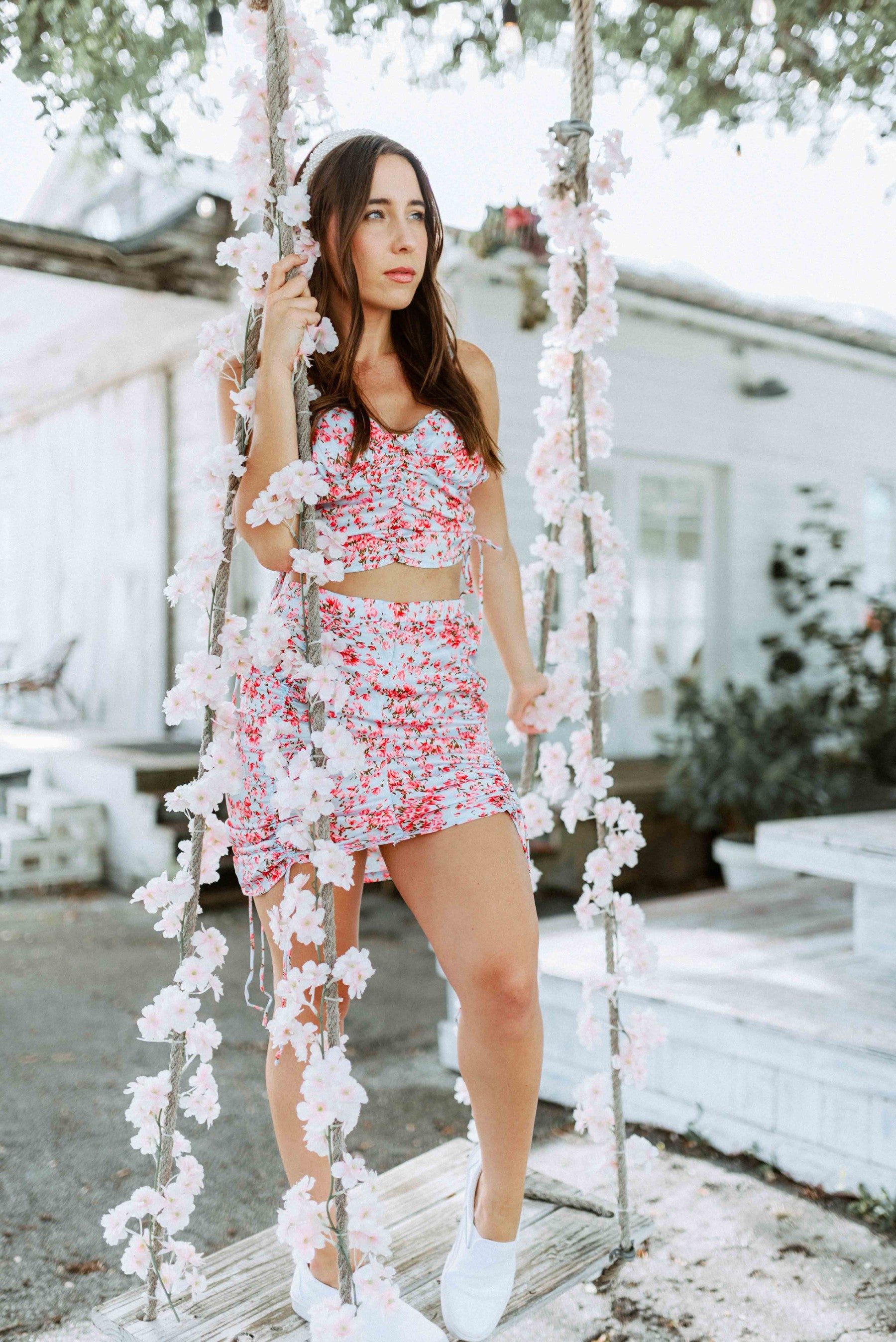 Brunette modeling a floral print matching mini scrunch skirt set in light blue and pink for Scarlette The Label, an online fashion boutique for women.