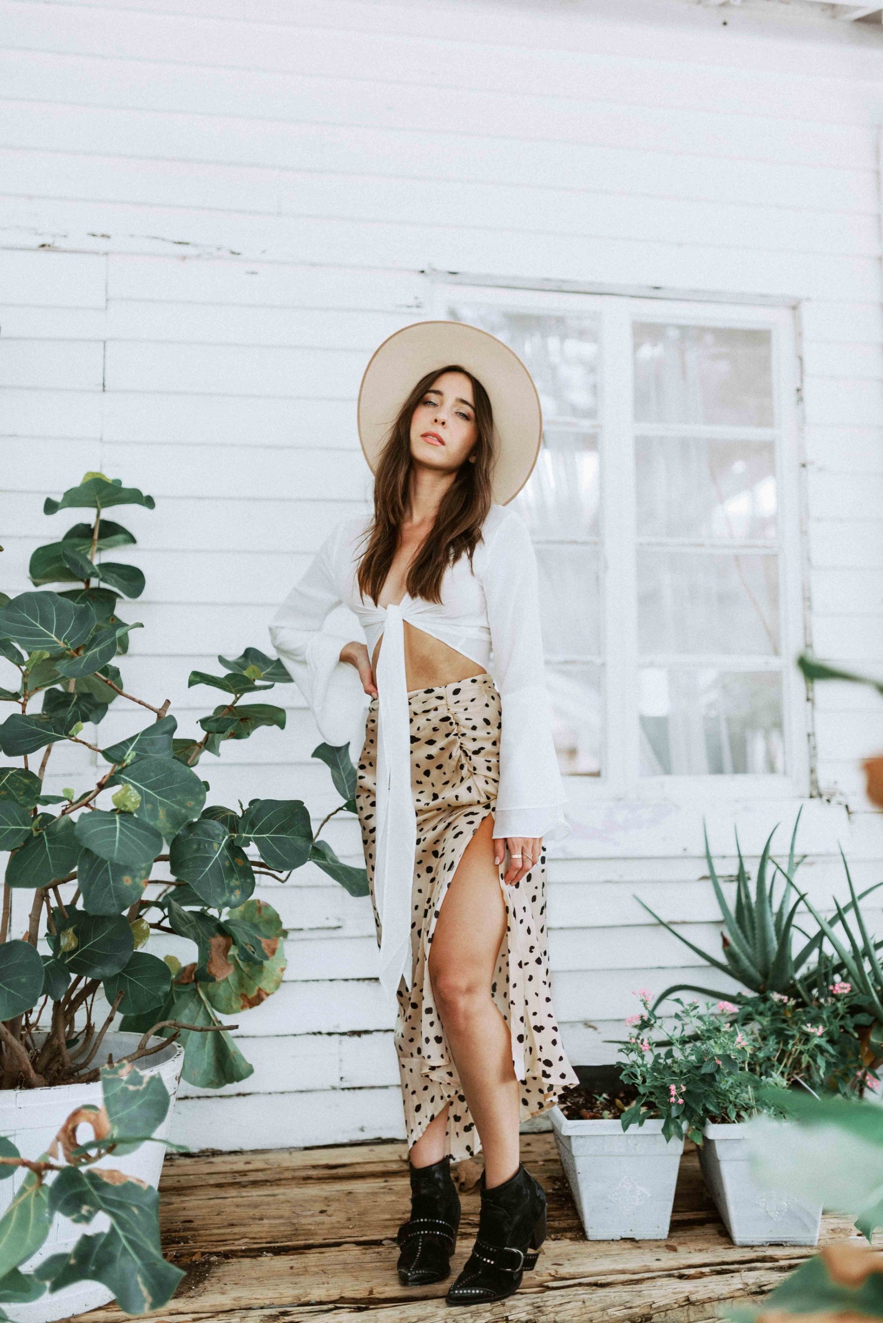 Brunette girl models white flared sleeve tie top and animal print maxi skirt for Scarlette The Label, an online fashion boutique for women. Paired with wide-brimmed rancher hat and black boots.