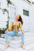 Load image into Gallery viewer, Brunette models yellow (mustard) crop tie top for Scarlette The Label, an online fashion boutique for women. Crop tie top has flared puff sleeves. Paired with light wash denim boyfriend jeans.