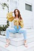 Load image into Gallery viewer, Brunette models yellow (mustard) crop tie top for Scarlette The Label, an online fashion boutique for women. Crop tie top has flared puff sleeves. Paired with light wash denim boyfriend jeans.