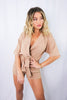 Blonde girl models tan collared romper for Scarlette The Label, an online fashion boutique for women. The romper is short sleeve and has a plunging collared neckline and adjustable waist strings.