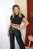 Blonde girl models an open back crop top in black and faux leather pants for Scarlette The Label, an online fashion boutique for women. The crop top is an open back string crop top in black paired with faux leather pants and a gucci belt.